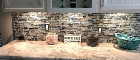 A kitchen with white cabinets, a marble countertop, a glass backsplash, and a sign indicating a stress-free zone.