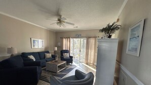 A living room with a blue sofa, a grey armchair, a coffee table, a ceiling fan, and a refrigerator. - Close enough to the beach but far enough from all of the noise! No pet fee! (Myrtle Beach,)