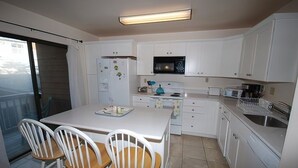 Una cuina compacta amb armaris blancs, microones, nevera i zona de menjador amb taula i cadires.