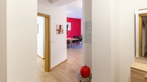 Ein Flur mit einer Holztür, einer roten Wand und einem Essbereich im Hintergrund.