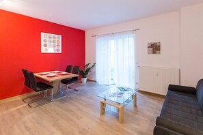 A modern living room with a red accent wall, a dining area with a table and chairs, a glass coffee table, and a sofa. - Lovely apartment in the historic center of Bolzano! (Bolzano)