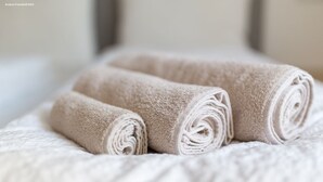 Drei gerollte Handtücher auf einem Bett mit einer strukturierten weißen Bettdecke.