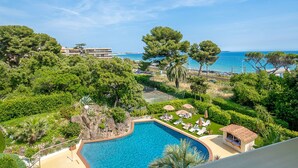 Zona de piscina con sillones de descanso, una cabaña pequeña y vistas al mar y edificios.