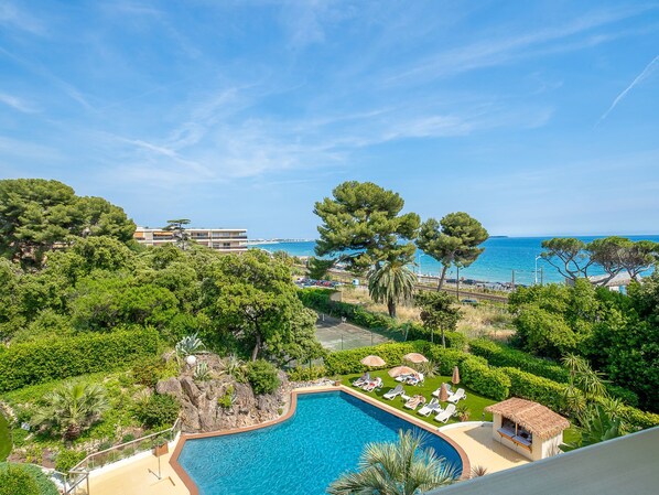 Ein Poolbereich mit Liegestühlen, einer kleinen Hütte und Blick auf das Meer und die Gebäude.