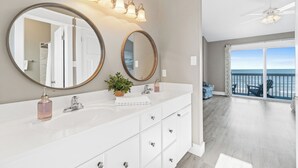 A modern bathroom with two large mirrors, a white vanity, and a plant. It features a balcony with a view of the ocean. - Direct Beachfront, gorgeous sunsets, gated community, north Cape near state park (Port St. Joe)