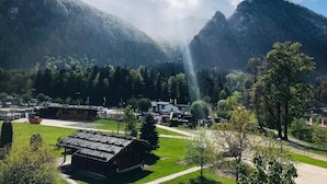 A rural setting with a small building, possibly a guesthouse, surrounded by lush greenery and mountains in the background.