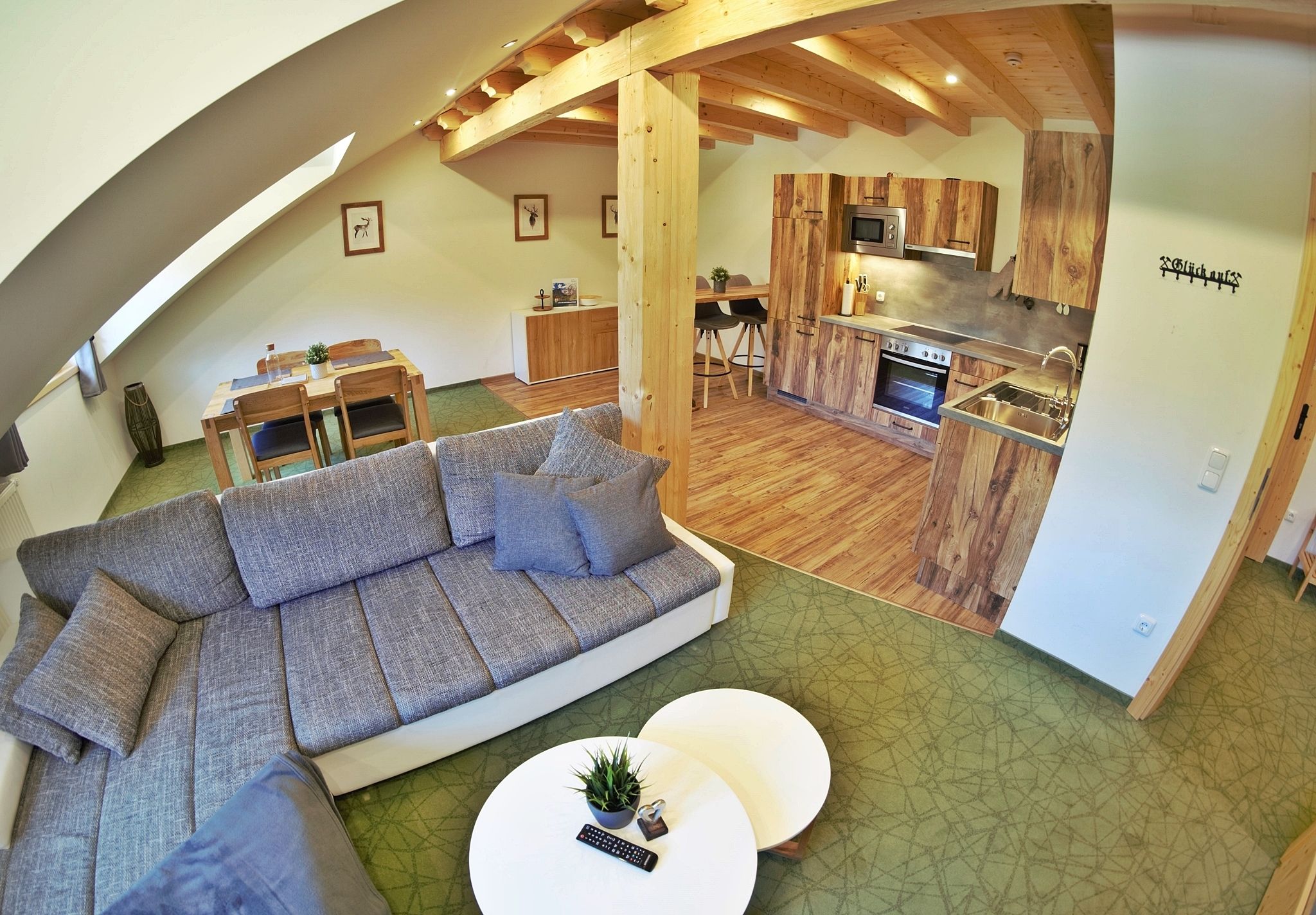 Een moderne loft-achtige woonruimte met een grote hoekbank, een eethoek en een keuken met houten kastjes.