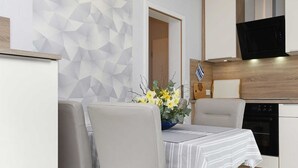 Eine moderne Küche mit Mikrowelle, Herd und Geschirrspüler. Ein Essbereich mit Tisch und Stühlen lädt zum Verweilen ein, und eine Wand mit geometrischen Mustern sorgt für eine stilvolle Atmosphäre.