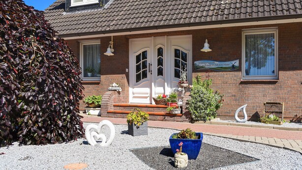 Ein zweistöckiges Haus mit Ziegeldach, Backsteinfassade und einer Veranda mit Blumentöpfen und einer Bank.
