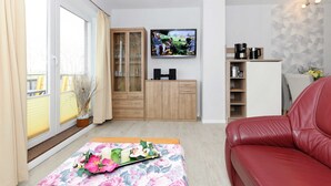 Ein modernes Wohnzimmer mit einem roten Ledersofa, einem Holzschrank, einem Fernseher und einer Kaffeestation.