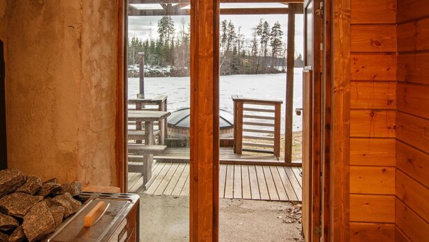 Une cabane en bois avec une porte en verre donnant sur une terrasse extérieure équipée d’une table et de chaises.