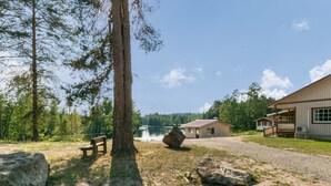 Un chalet au bord du lac, avec un grand rocher au premier plan, une table de pique-nique et un bâtiment doté d’une véranda.