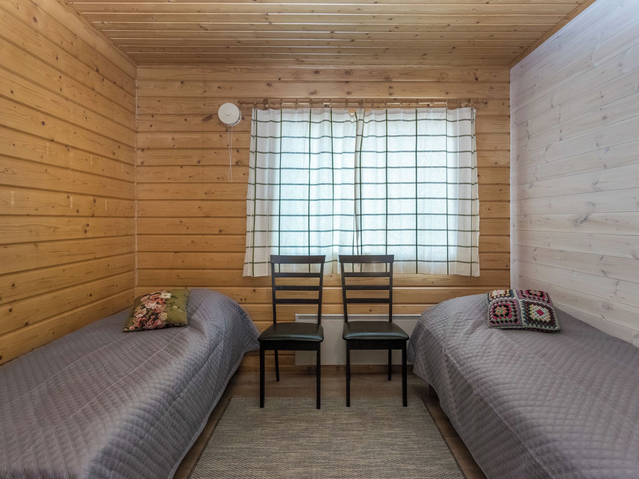 A cabin room with two beds, a window with curtains, a radiator, and a rug.