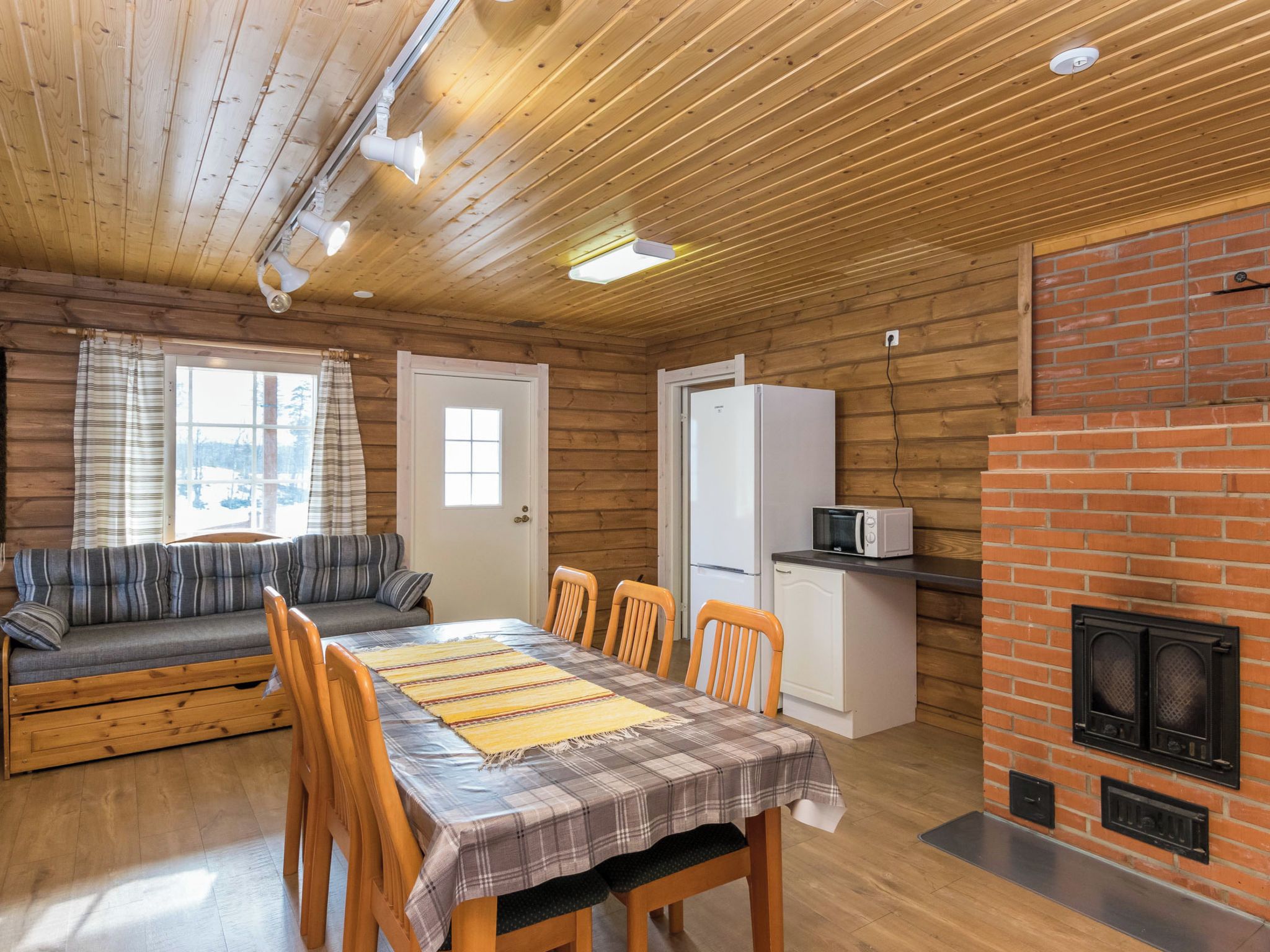 A cozy cabin interior with a dining area, a sofa, a fireplace, and a kitchen.