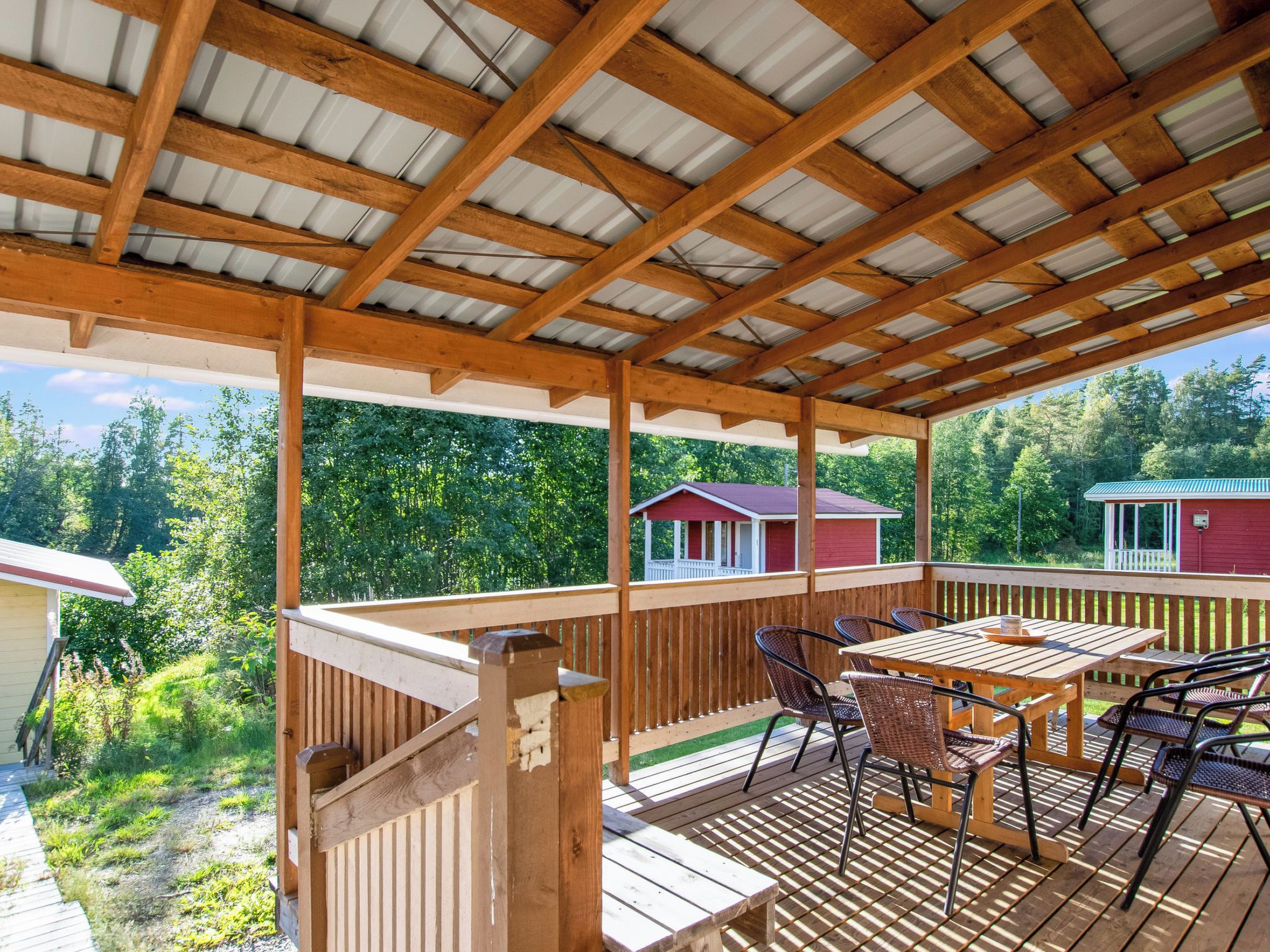 Eine überdachte Holzterrasse mit einem Holztisch und Stühlen, umgeben von einem Holzbalkon.