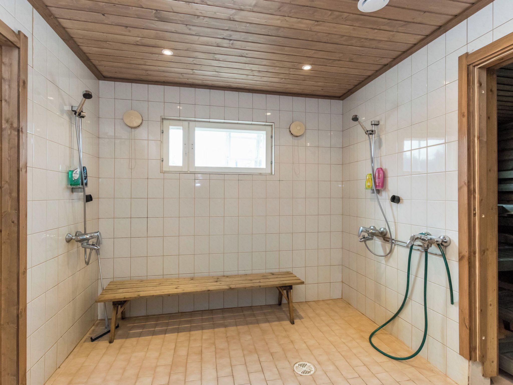 A shower area with a bench, tiled walls, and a wooden ceiling.