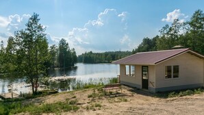 Une cabane au bord d’un lac, avec un quai, entourée d’arbres et sous un ciel dégagé.