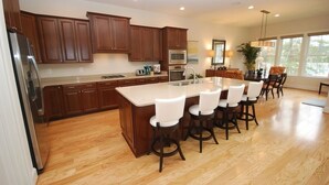 Una cocina moderna con armarios de madera, una isla central con taburetes, un refrigerador y un comedor con sillas y una mesa.