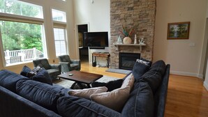Una sala de estar con chimenea de piedra, un televisor de pantalla plana y un ventanal con vistas a una terraza.