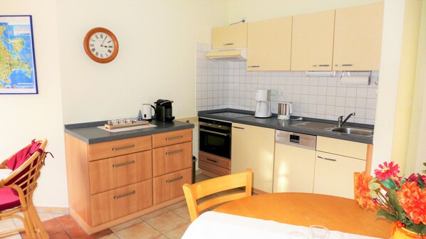 A compact kitchen with wooden cabinets, a built-in oven, a dishwasher, and a coffee maker.