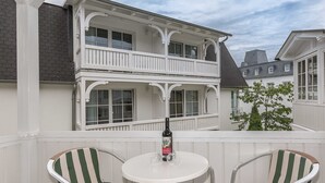 Ein weißer Balkon mit Tisch und zwei gestreiften Stühlen, mit Blick auf eine Wohngegend.