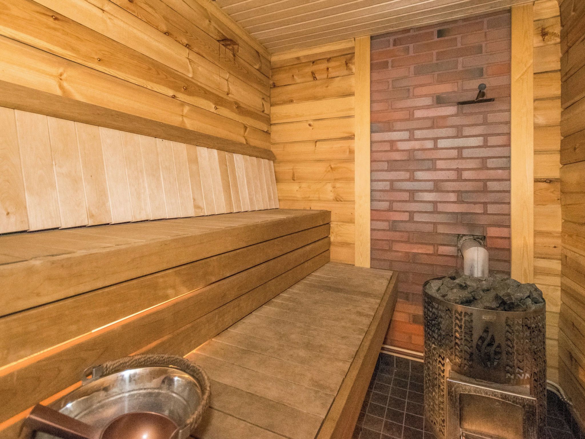 Una sauna con bancos de madera, pared de ladrillo y estufa de piedra.