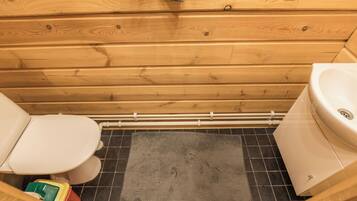 Une salle de bain rustique, aménagée dans une cabane en bois, avec des toilettes, un lavabo et un espace douche.