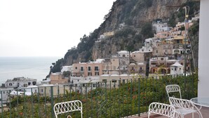 A terrace with white metal chairs and a table overlooking a coastal town with buildings on a hillside. - Positano Center - Guest 4+2 People in 2 Bedrooms, 2 Bathrooms - AC and WiFi free (Positano)