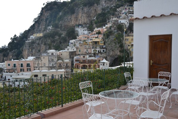 Une terrasse avec des chaises et une table en métal blanc, donnant sur une colline parsemée de bâtiments aux couleurs vives.