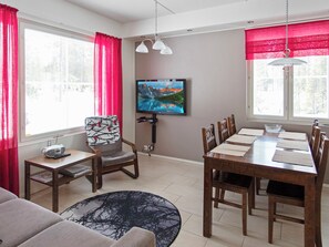 A modern living room with a dining area, a flat-screen TV mounted on the wall, and a window with red curtains. - Yllästar 3 as 506 by Interhome (Äkäslompolo)
