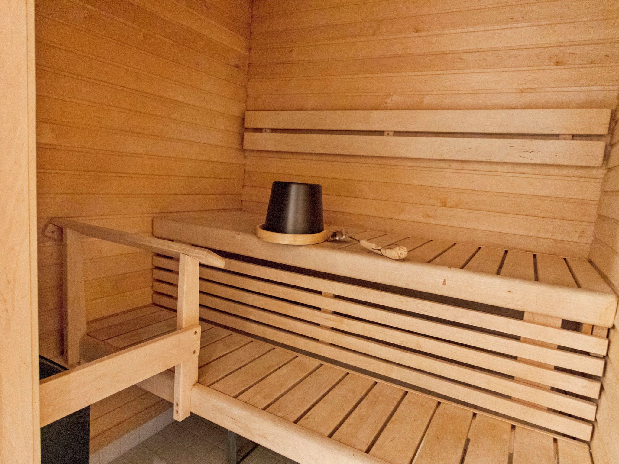 Una sauna con bancos de madera y un recipiente negro sobre uno de ellos.