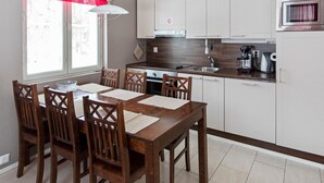 Een moderne keuken met witte kastjes, een houten eettafel en een rood jaloeziestoel.
