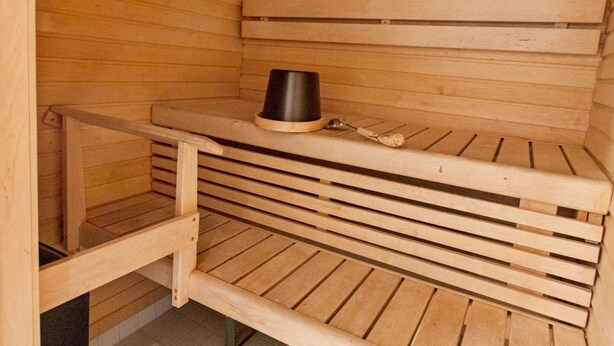 Een sauna met houten banken en een zwarte container op de bank.
