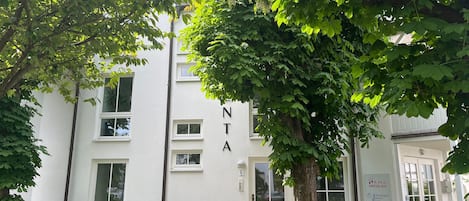 Un edificio blanco con las letras 'NTA' en la fachada, rodeado de follaje.