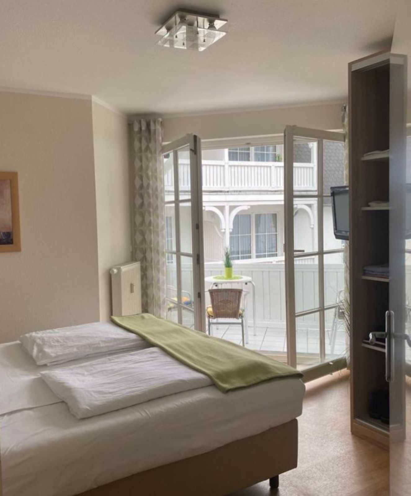A hotel room with a bed, a TV, a chair, and a balcony with a view of a building.