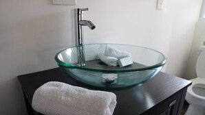 A bathroom with a glass bowl sink, a towel on the counter, and a toilet in the background. - Experience the passion of hospitality, cleaning, and good location! (Tampa)