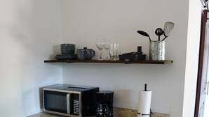 A compact kitchen with a microwave, coffee maker, and a small refrigerator. There is a shelf above the counter holding various kitchen items. - Experience the passion of hospitality, cleaning, and good location! (Tampa)