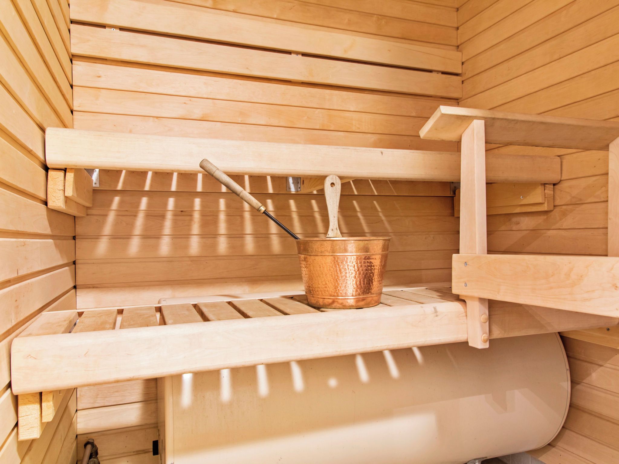 Una sauna con bancos de madera y un cubo de cobre.