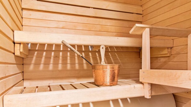 A sauna with wooden walls and a metal bucket with a wooden handle.