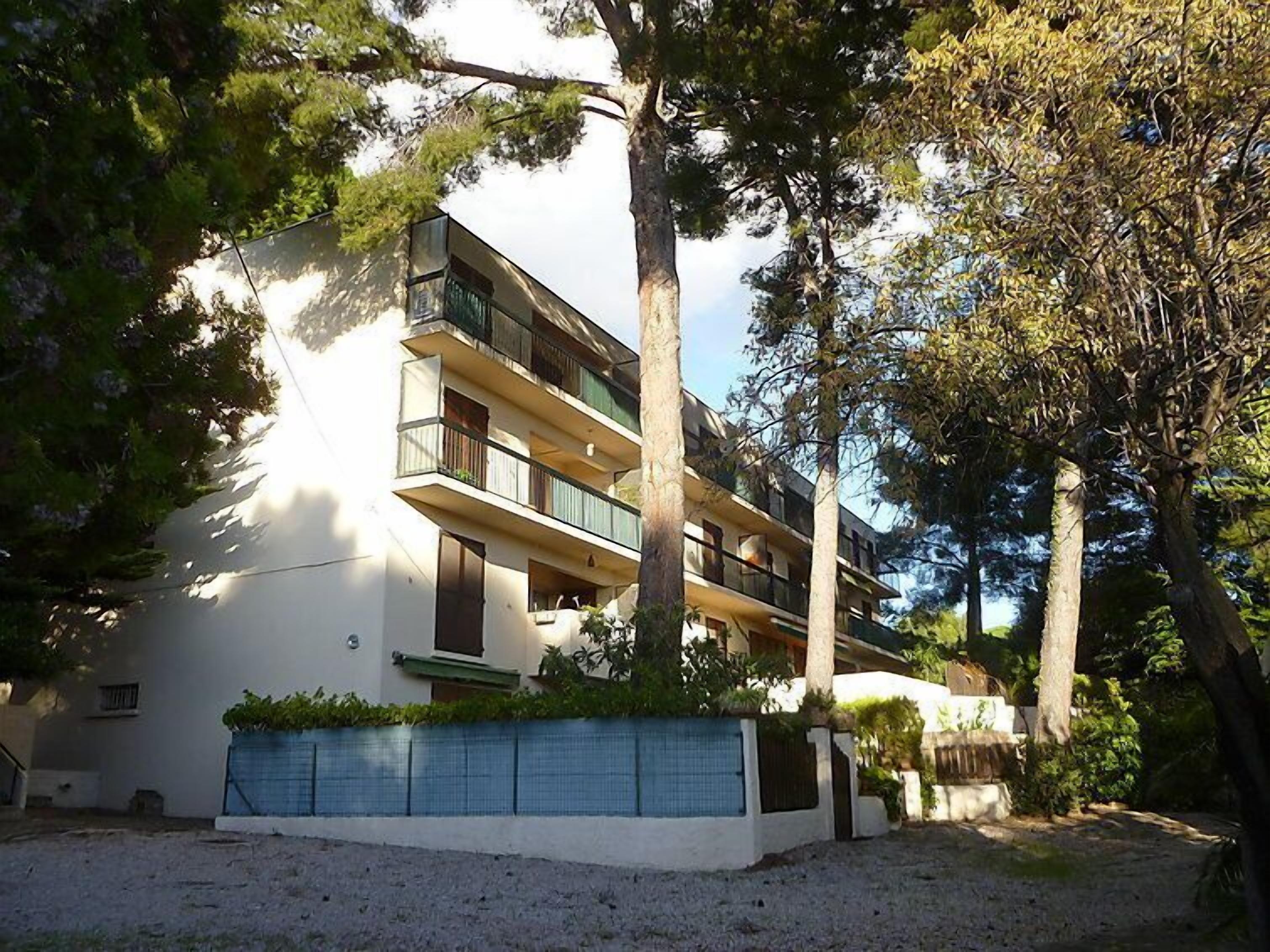 A multi-story building with balconies, surrounded by trees.