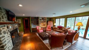 A cozy living room with a fireplace, bookshelves, and a view of a swimming pool. - Mountain House -  A private rustic oasis with goats!  (New Hope)