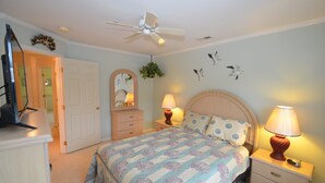 Een slaapkamer met een bed, nachtkastjes, een plafondventilator, een dressoir, een spiegel en decoratie aan de muur.