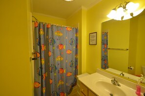 A bathroom with a yellow wall, a white sink, a mirror, and a shower curtain with fish patterns.