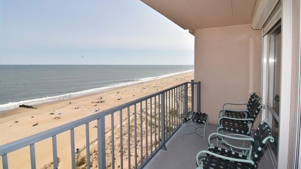 Ein Balkon mit Blick auf Strand und Meer. Vier Metallstühle und ein Tisch sind vorhanden.