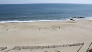 Ein weiter Sandstrand mit freiem Blick auf den Ozean und einer Betonbarriere.