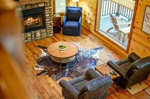 Interior acogedor de una cabaña con chimenea de piedra, asientos de cuero, una mesa redonda de madera y vistas a la terraza.