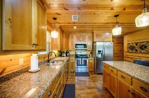 A kitchen with wooden cabinets, granite countertops, stainless steel appliances, and pendant lighting.