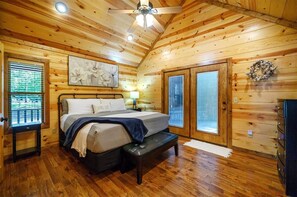 Een slaapkamer met houten lambrisering, een bed, een bankje, een plafondventilator en een raam met jaloezieën.