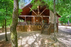 Een chalet met een houten terras, een stenen muur en een trap naar de ingang.