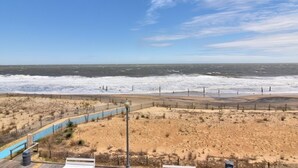 A beach view with a wooden boardwalk, a fence, and a stormy sea.